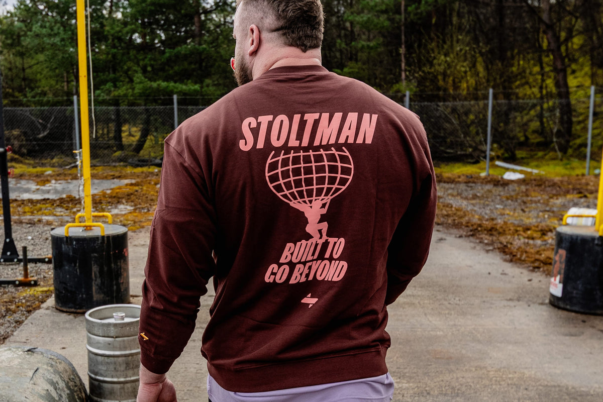 Man wearing a maroon jumper with 'Stoltman' branding outdoors.